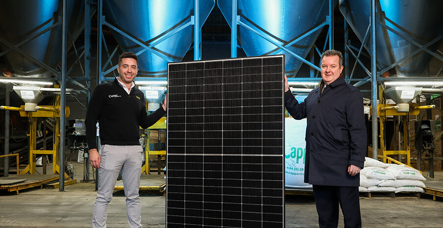 Two men are standing on each side of a solar panel inside a warehouse