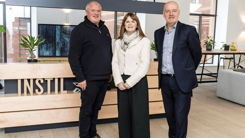 Two men and a woman are standing in an office space, posing for a photo together 