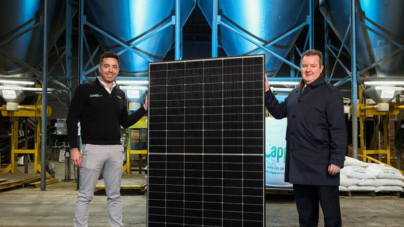 Two men are standing on each side of a solar panel inside a warehouse